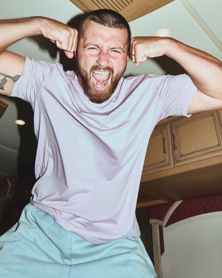 Athlete flexes both arms and shouts wearing a light Under Armour t shirt indoors.