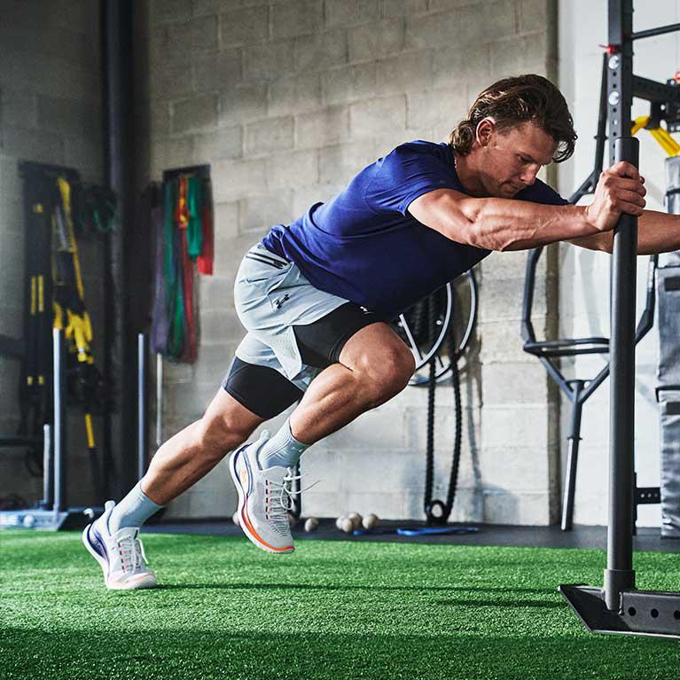 A man working out at the gym, wearing a blue shirt, white shorts and trainers, with a focused expression on his face.