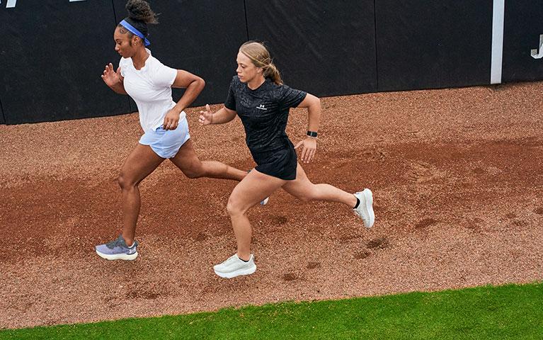 Two women in athletic wear running through a track field 