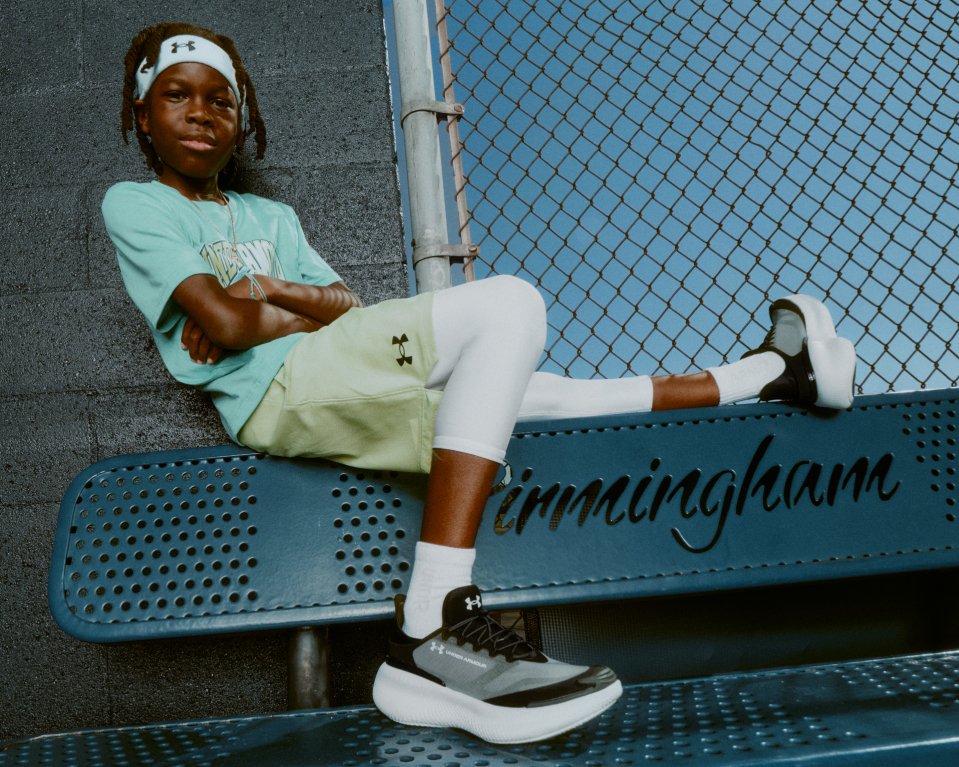 Athlete lounges on a bench wearing Under Armour headband and sneakers with arms crossed and one leg extended.